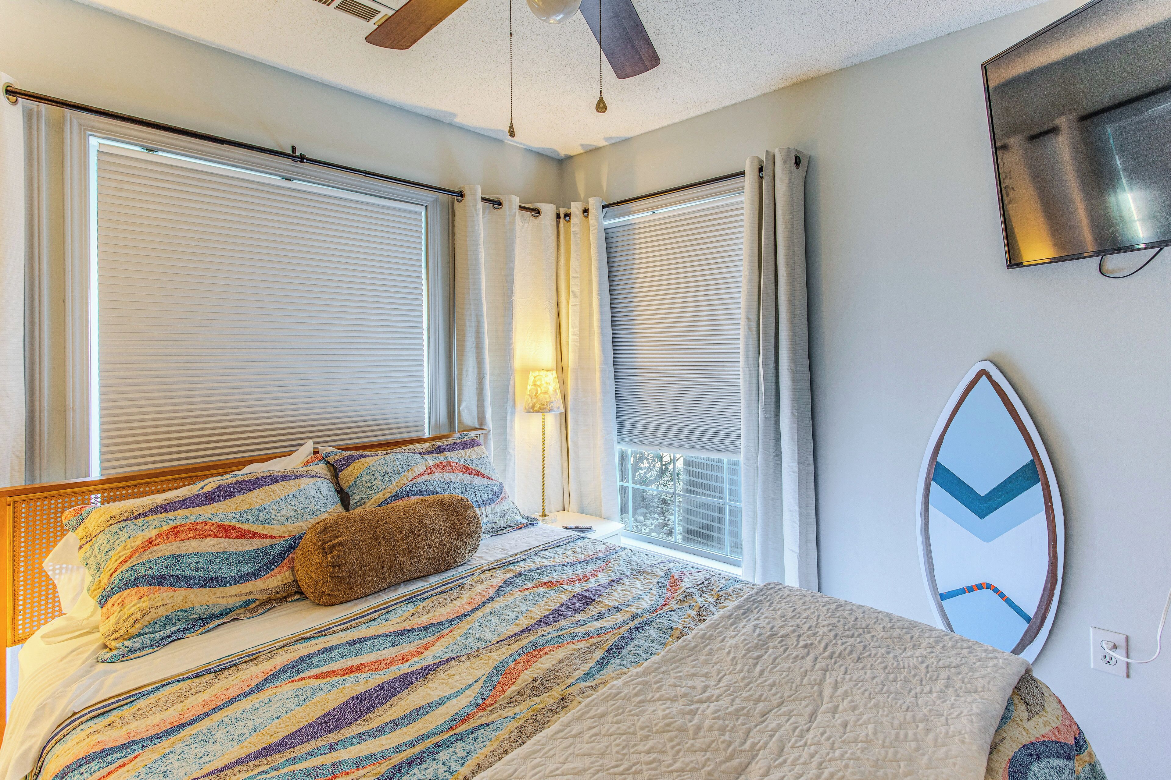 Ein Schlafzimmer mit Bett, Deckenventilator, montiertem Fernseher und einem Surfbrett an der Wand.