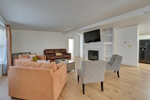 A spacious living room with a fireplace, a television, and a kitchen area. - Game Room + Easy ECU Access: Greenville Getaway (Greenville)