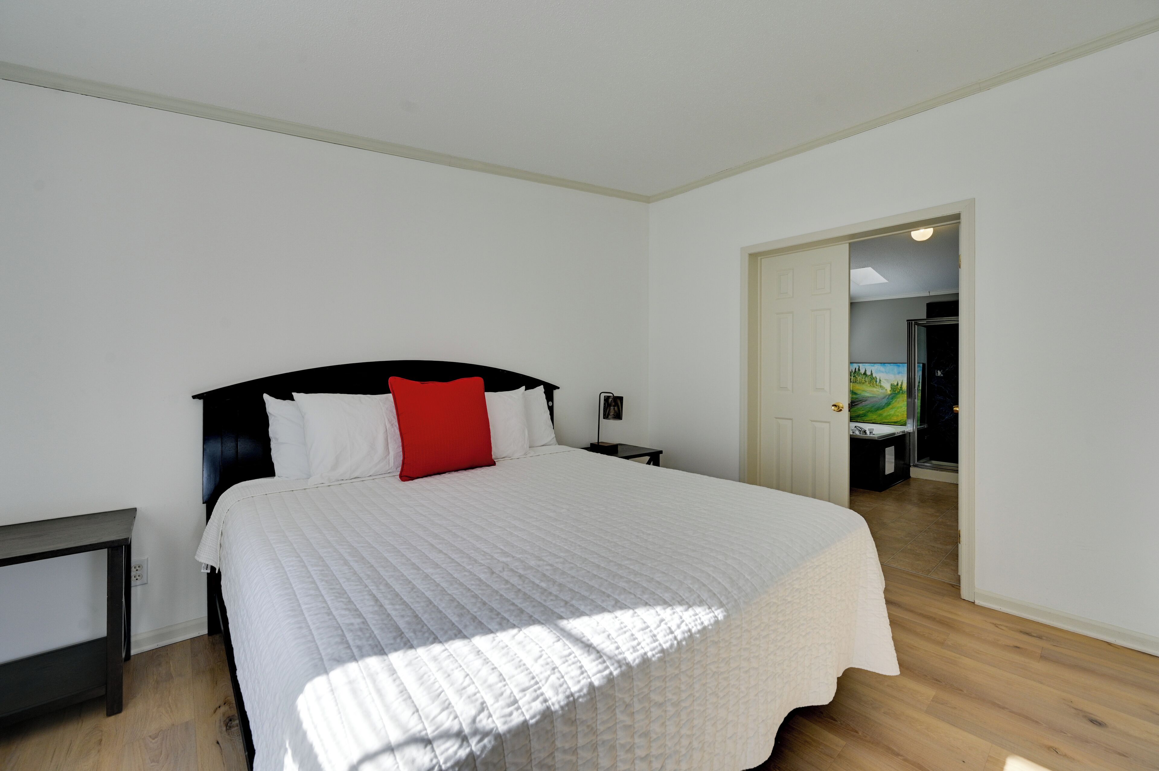 Een slaapkamer met een groot bed, een nachtkastje, een bureau en een deur die naar een andere kamer leidt.