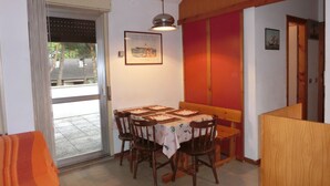 A dining area with a table set for four, wooden chairs, a hanging light fixture, and a framed picture on the wall. - Cozy Apartment With Swimming Pool Access (San Michele al Tagliamento)