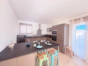 A modern kitchen with a central island, bar stools, and a view of the outside. - Rooftop villa les oliviers (Prunelli-di-Fiumorbo)
