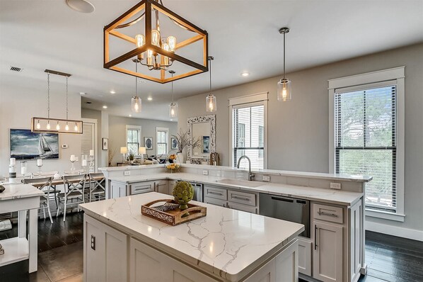 A spacious kitchen with a central island, pendant lighting, and a large window providing natural light. - 30A Seaclusion- Private Heated Pool Gulf Views Golf Cart Included (Seagrove)