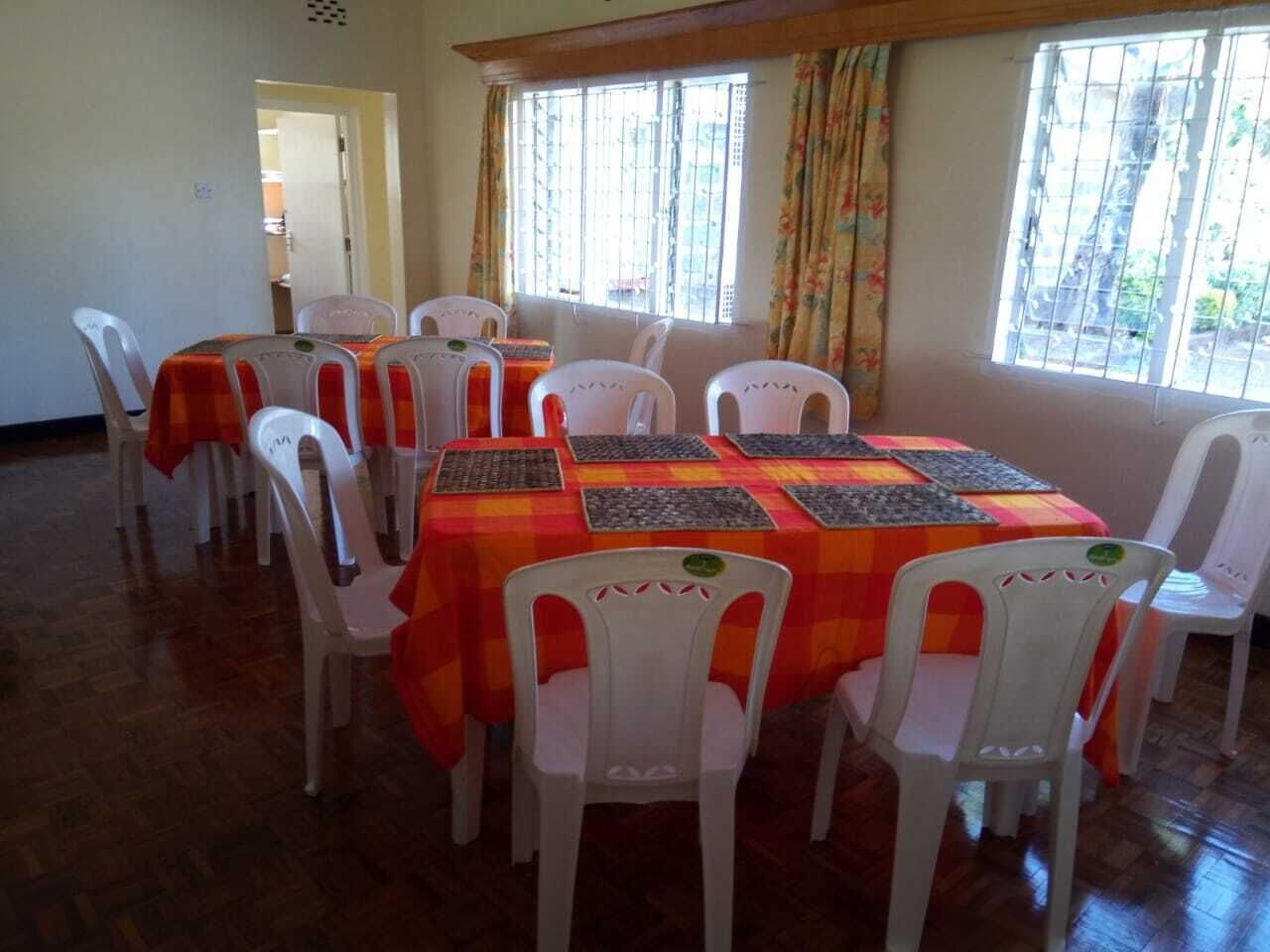 A dining area with white plastic chairs and tables covered with orange and red checkered tablecloths.