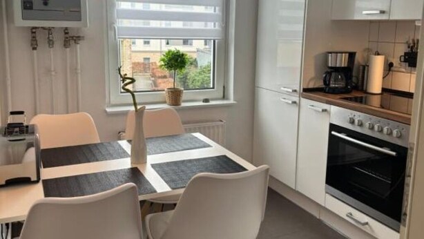 A modern kitchen with white cabinets, a built-in oven, and a dining area with a table and chairs. - Vacation apartment Hansetraum Lübeck (Lübeck)