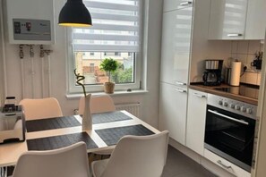 Et moderne køkken med lyse skabe, indbygget ovn og spiseplads med bord og stole.