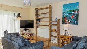 A living room with a wooden TV stand, a flat-screen TV, a wooden table, and two grey sofas.