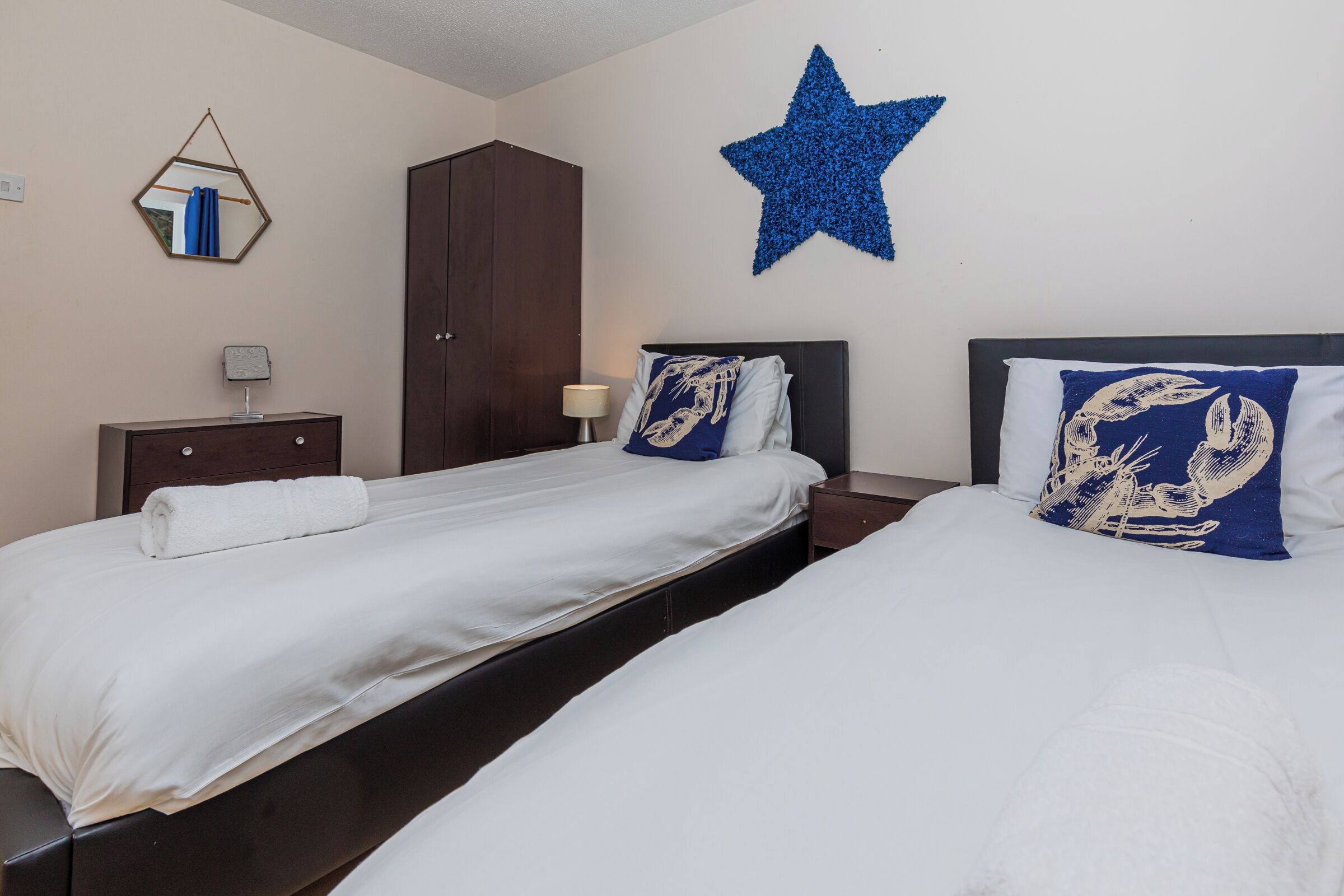 Habitación de hotel con dos camas, un armario, una mesita de noche, una lámpara y una estrella decorativa en la pared.