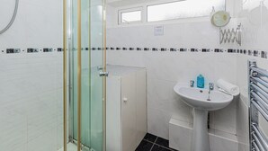 A bathroom with a glass shower enclosure, a white sink with a mirror, and a tiled floor.