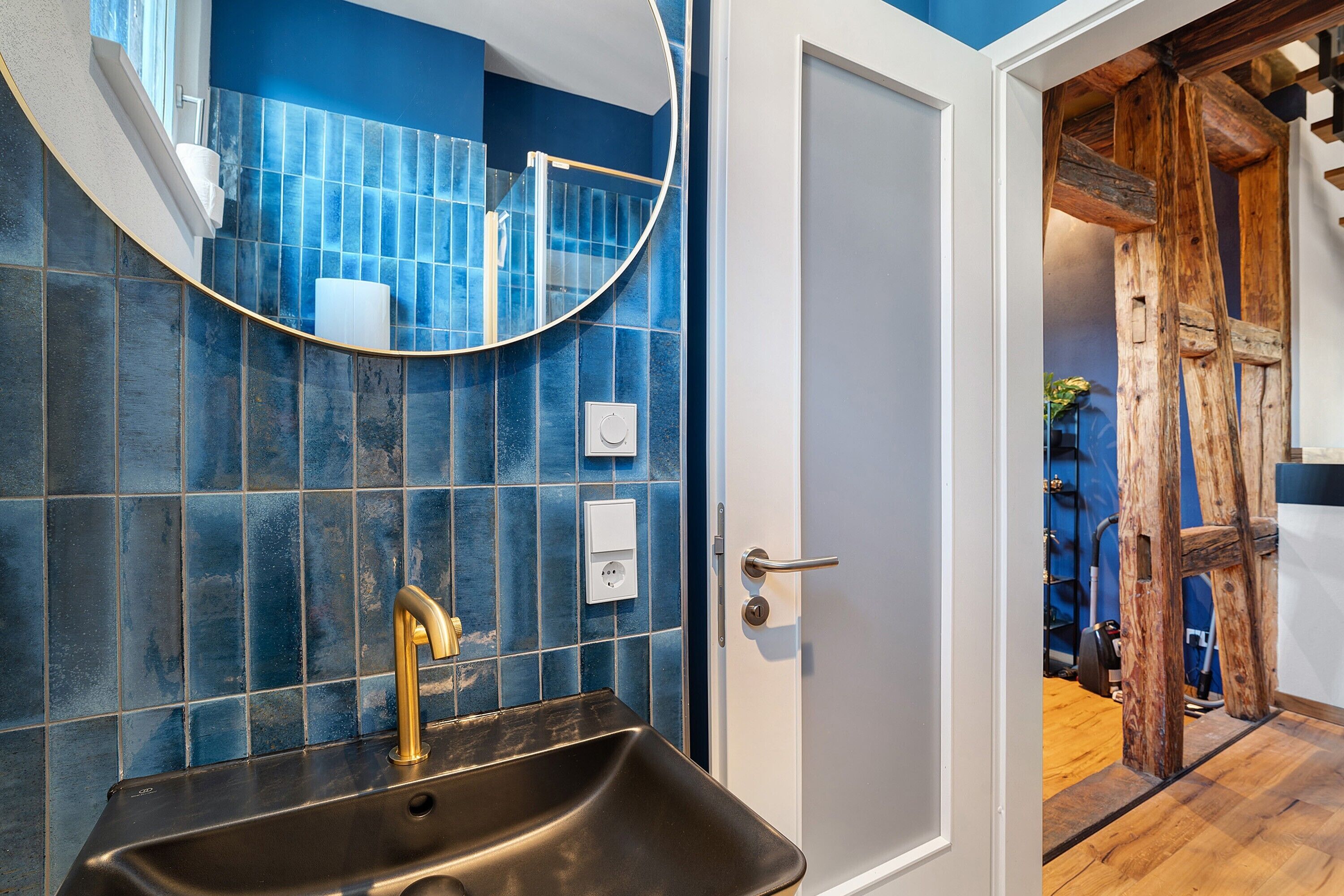 A bathroom with a black sink, a gold faucet, a blue-tiled wall, and a wooden door frame.