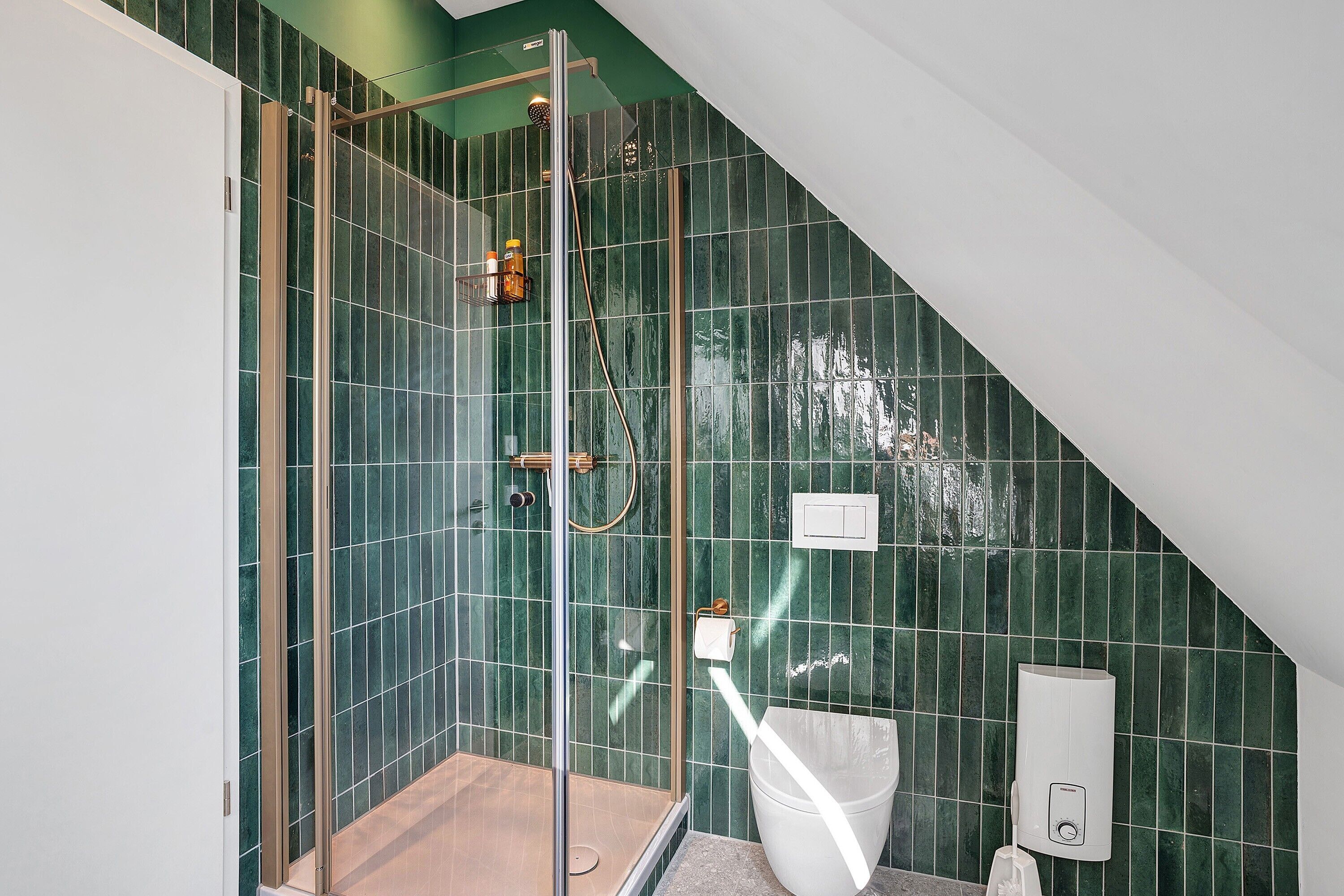 A modern bathroom with a glass-enclosed shower, a white toilet, and green-tiled walls.