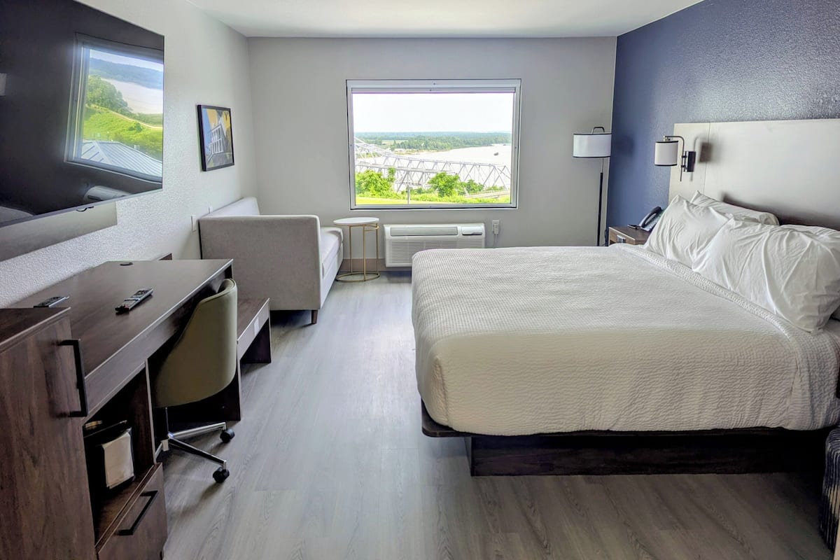 Una habitación de hotel con cama, escritorio, silla, ventana con vistas y televisión.