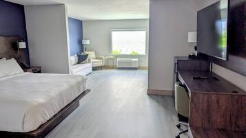 A hotel room with a bed, a desk, a chair, a television, a window, and a lamp.