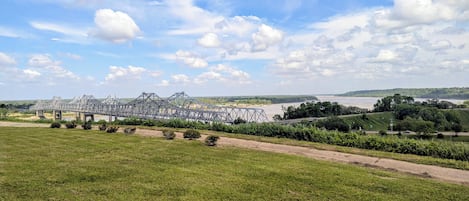Eine große Metallbrücke überspannt einen Fluss, umgeben von grünen Feldern und Bäumen.