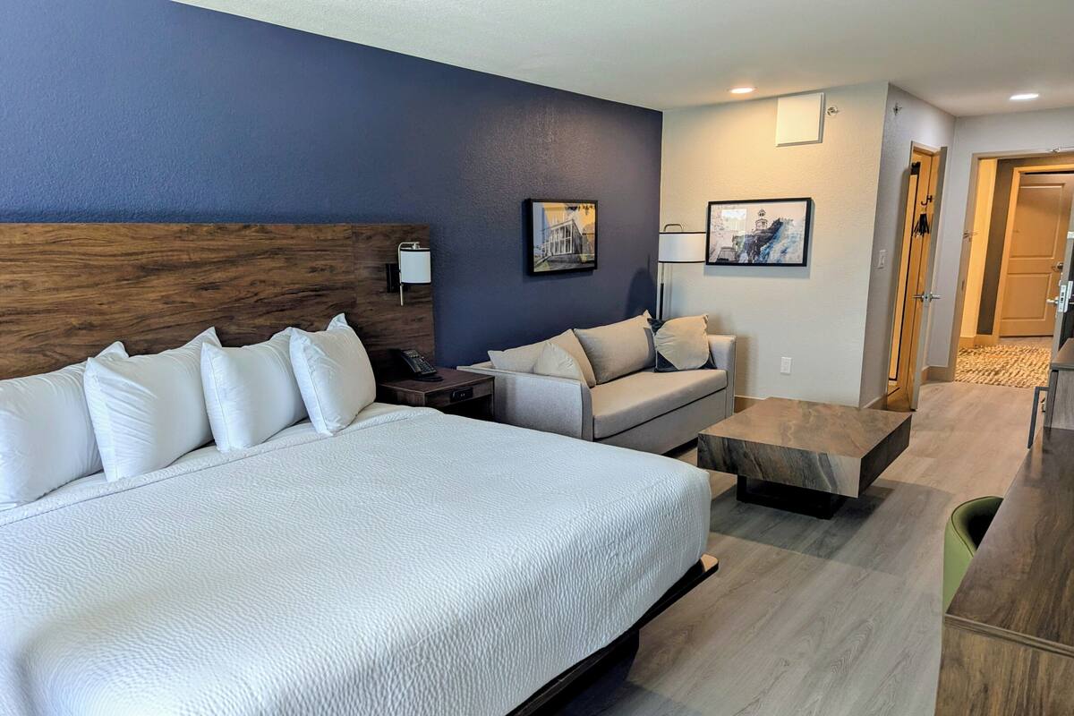Una habitación de hotel con una cama grande, un sofá, una mesita de café y un escritorio con una lámpara.