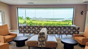 A lounge area with a view of a park and water, featuring sofas, a table, and a coffee table. - The Hotel Vue (Natchez)