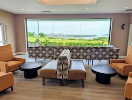 A lounge area with a view of a park and water, featuring sofas, a table, and a coffee table.