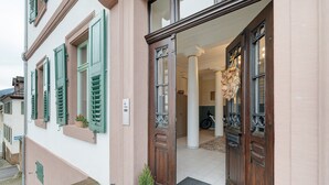 Ein Gebäudeeingang mit einer Holztür, grünen Fensterläden und einem Blumentopf.