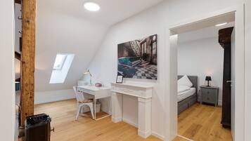 A bedroom with a bed, a desk, a chair, a nightstand, and a painting.