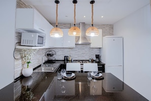 Une cuisine moderne dotée d’un îlot central, de meubles blancs, d’un four à micro-ondes, d’une cuisinière et d’un réfrigérateur.