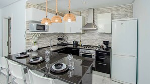 Une cuisine moderne dotée d’un îlot central, de meubles blancs, d’une hotte en acier inoxydable et d’un four à micro-ondes encastré.