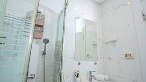 Une salle de bain moderne avec une douche à l’italienne en verre, un lavabo blanc et un grand miroir.