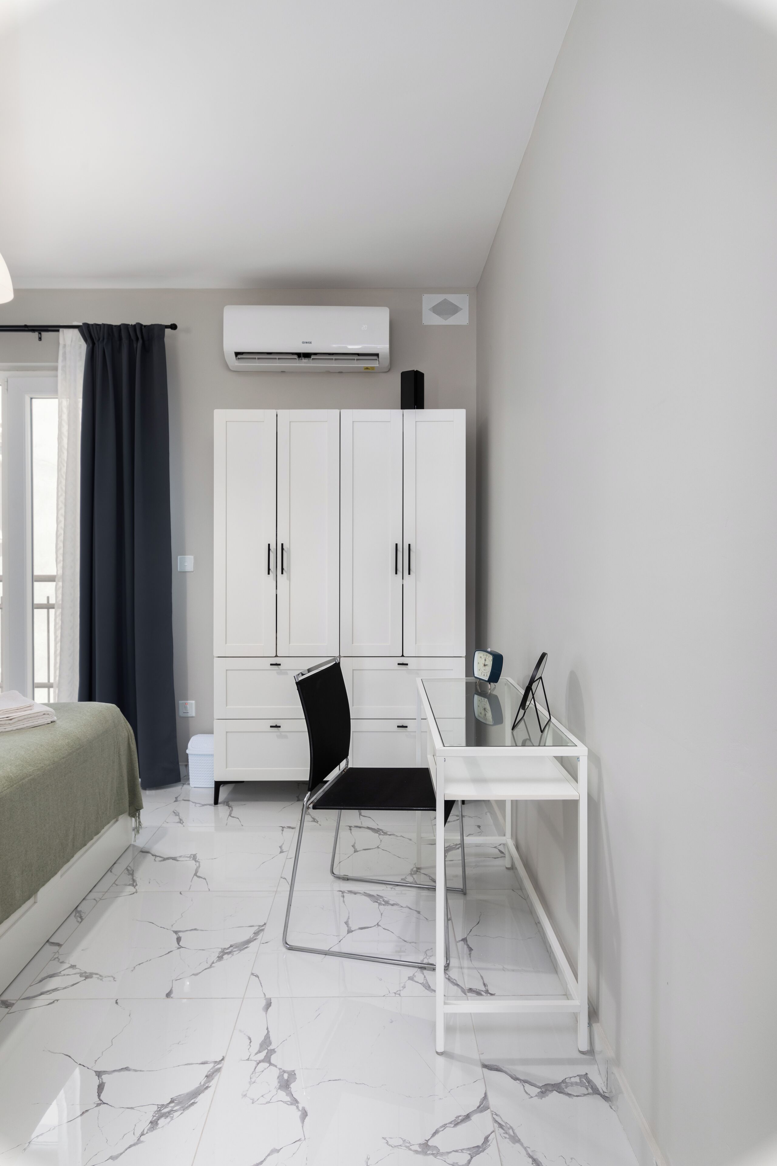 A bedroom with a bed, a desk, a wardrobe, and an air conditioning unit.