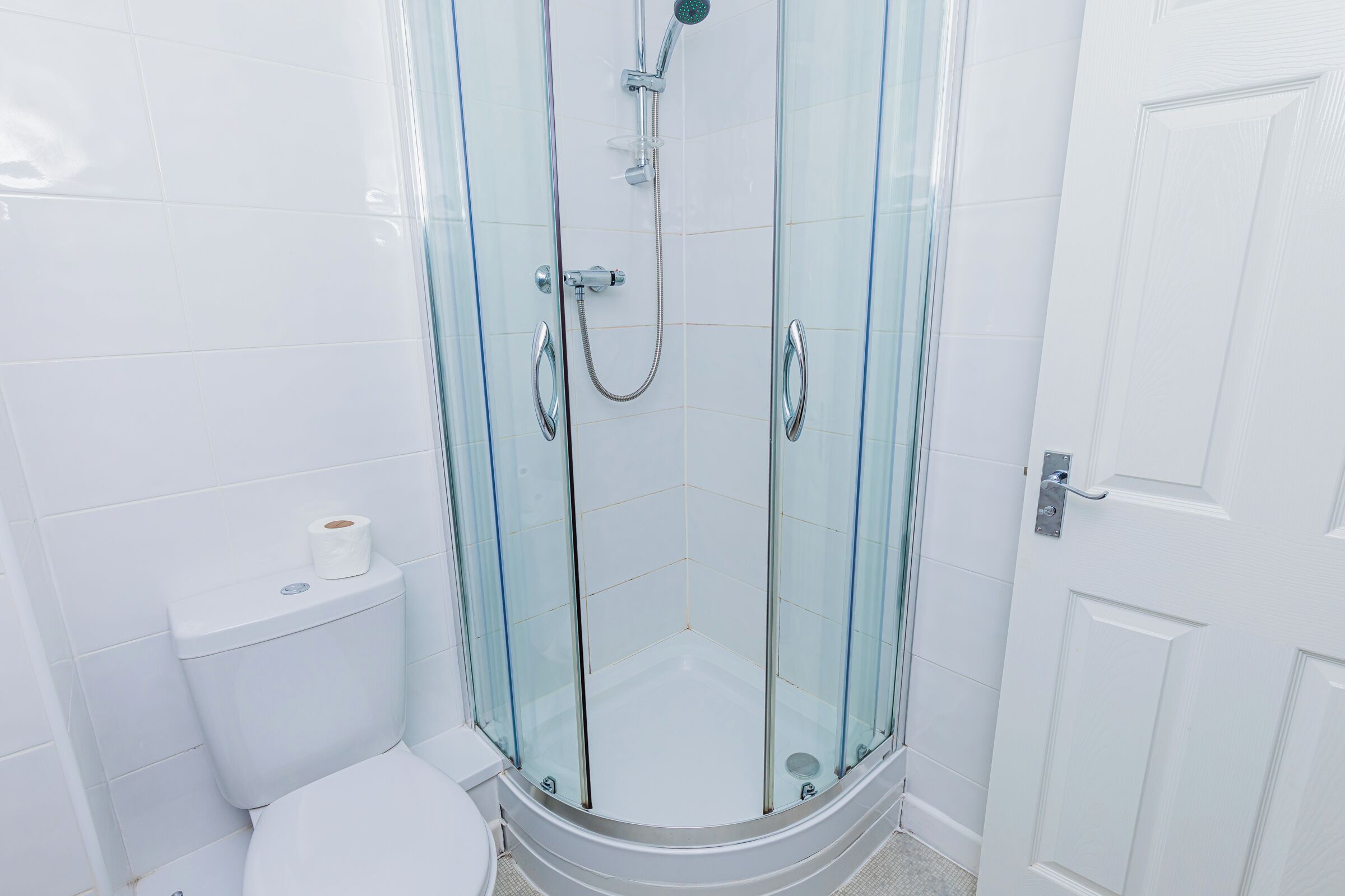 A glass-enclosed shower with a toilet to the left and a door to the right.