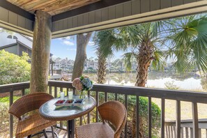 A covered outdoor area with wicker chairs and a table, overlooking a body of water and palm trees. - Lagoon view, central location, Parkside villa (Kiawah Island)