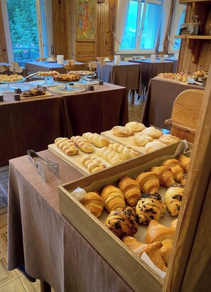 Eine Bäckertheke mit verschiedenen Backwaren und Brot, Holztische und ein Blick ins Freie durch große Fenster.