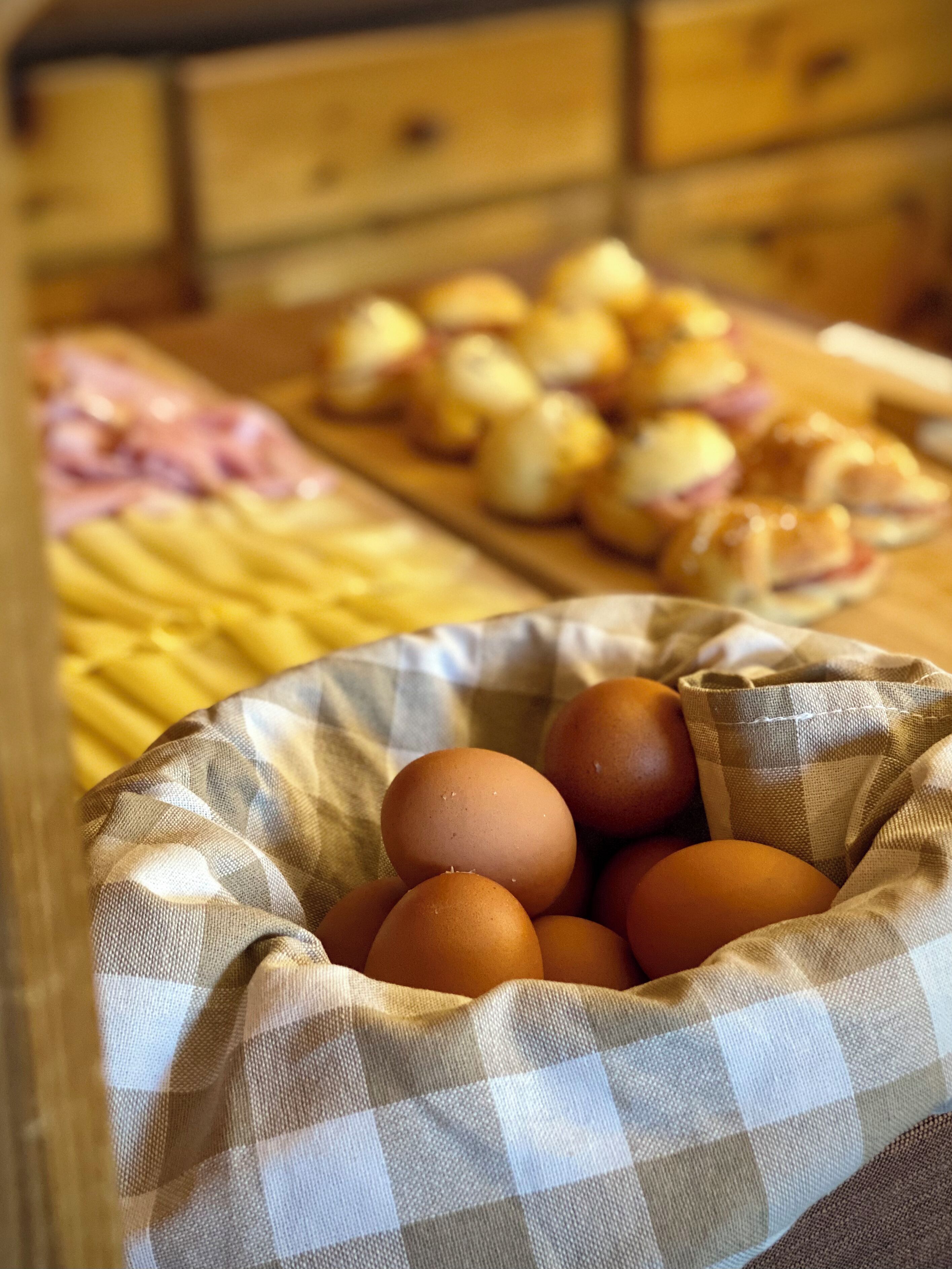 Une cuisine avec un sac à carreaux contenant des œufs, une planche à découper avec des pommes de terre coupées en tranches et, au fond, des armoires en bois.