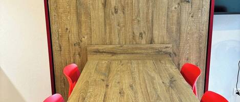 Una mesa de conferencias con cuatro sillas rojas y un panel de madera en una sala con suelo de baldosas.