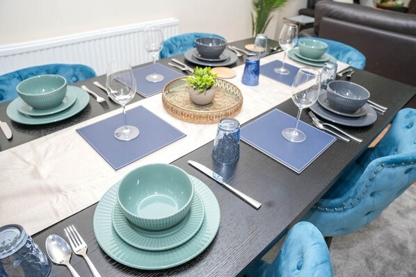 Une table à manger dressée avec de l’argenterie turquoise, des assiettes, des bols et des couverts, accompagnée de chaises bleues.