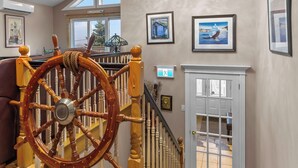 Una escalera con barandilla de madera, una rueda de barco y cuadros en las paredes.
