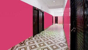 Ein Korridor mit gemustertem Boden, einer rosa Wand und einer schwarzen Tür mit Struktur.