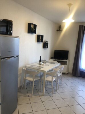 A compact living space with a kitchenette, a dining area, and a television. - Appartement 40m² 1 chambre, parking et balcon (Aix-les-Bains)