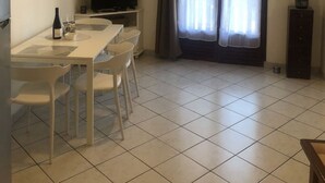 Ett kompakt bostadsutrymme med en matplats, en platt-TV, ett kylskåp och ett stort fönster med gardiner.