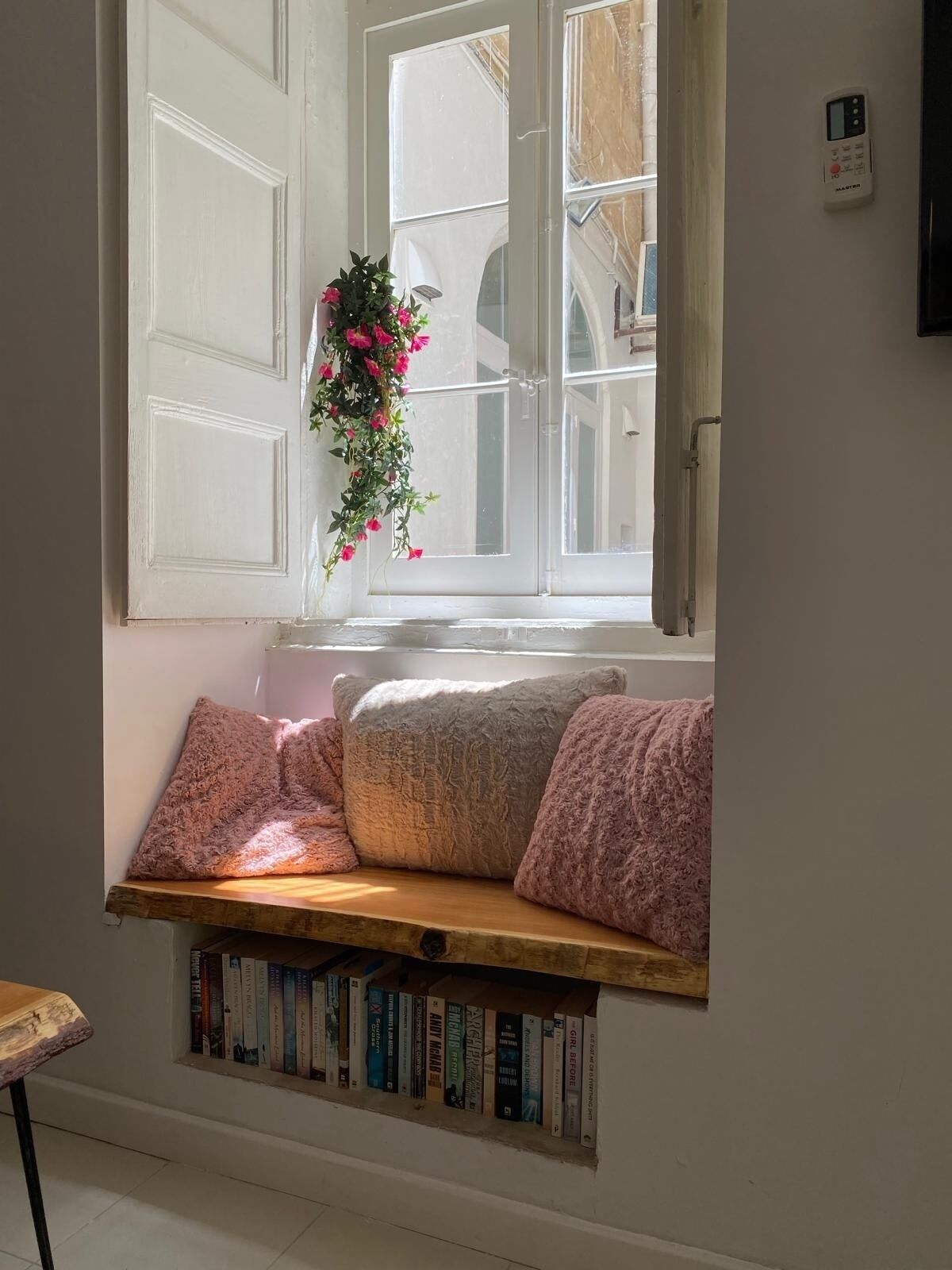 Un coin lecture confortable avec un banc intégré, une composition florale suspendue et une bibliothèque remplie de livres.