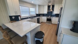 Een moderne keuken met witte kasten, een marmeren eiland en een zwarte prullenbak.
