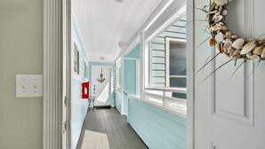 A hallway with light blue walls, white trim, and a white door with a seashell wreath. - Quail Hollow A8-1u 2 Bedroom Condo (St. Augustine)