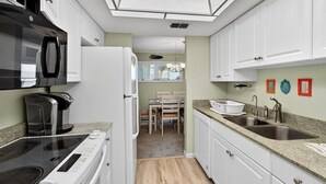 A compact kitchen with a built-in microwave, stove, and refrigerator. There is a dining area with a table and chairs visible through an open door. - Quail Hollow A8-1u 2 Bedroom Condo (St. Augustine)