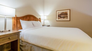 A neatly made bed with white linens, a wooden headboard, and two bedside lamps.