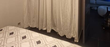 A bedroom with a bed, a curtain, and a view of a bathroom.
