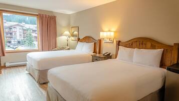 A hotel room with two beds, a window with a view of buildings and trees, a wooden headboard, bedside lamps, and a nightstand.
