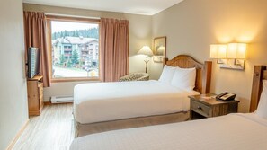 A hotel room with two beds, a TV on a stand, a lamp, a phone, and a view of buildings outside the window. - Cahilty #212 Hotel Room (Sun Peaks)