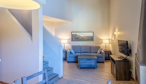 A modern living room with a staircase, a sofa, a coffee table, and a flat-screen TV.