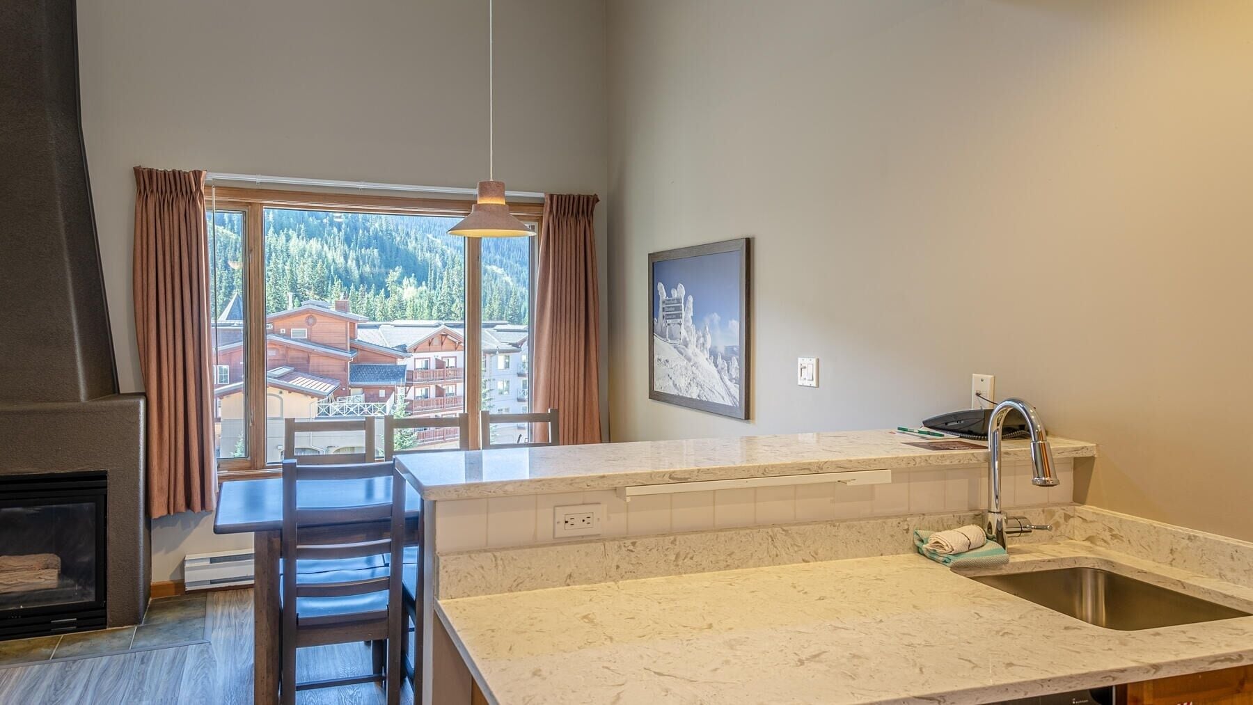A modern kitchen with a large window, a dining area with a chair, and a fireplace.