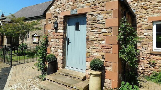 Una casa di pietra con una porta azzurra, un piccolo portico e un cartello che riporta la scritta 'Chapel Cottage'.