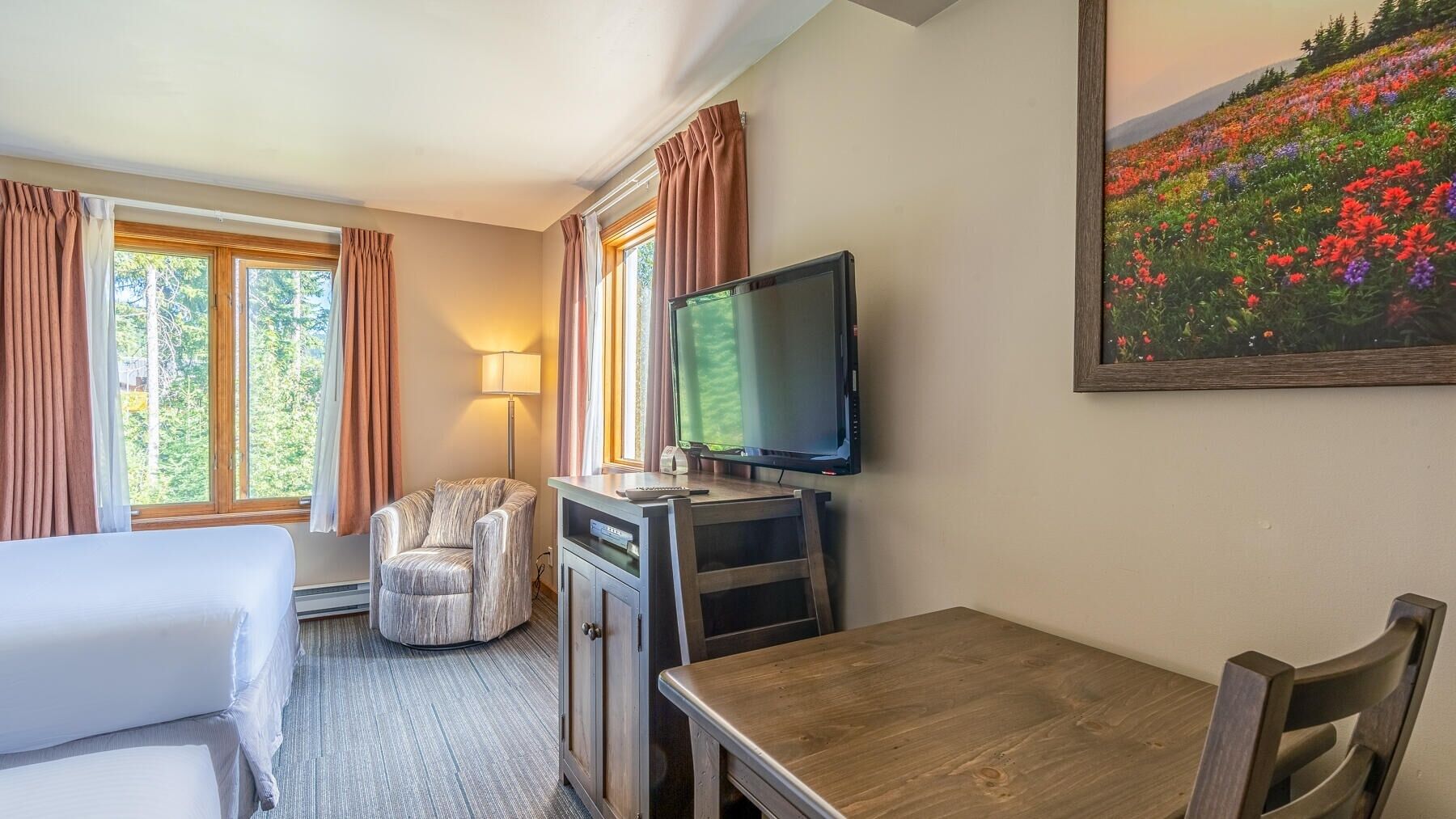Habitación de hotel con cama, escritorio con televisor, una silla y un cuadro de flores en la pared.