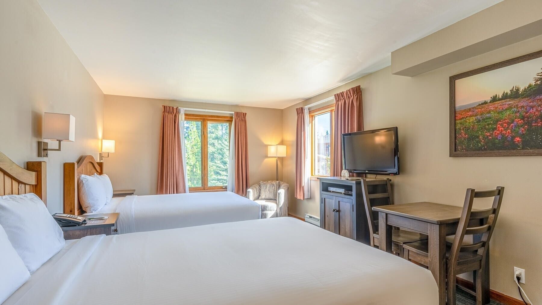 Habitación de hotel con dos camas, un escritorio con silla, un televisor y un cuadro en la pared.