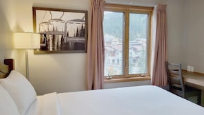 A hotel room with a bed, a desk, a chair, a lamp, and a window with curtains. - Cahilty #318 Hotel Room (Sun Peaks)
